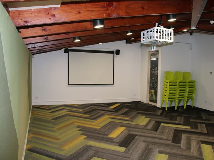 Timber-beamed room with herringbone carpet, projection screen, stacked green chairs