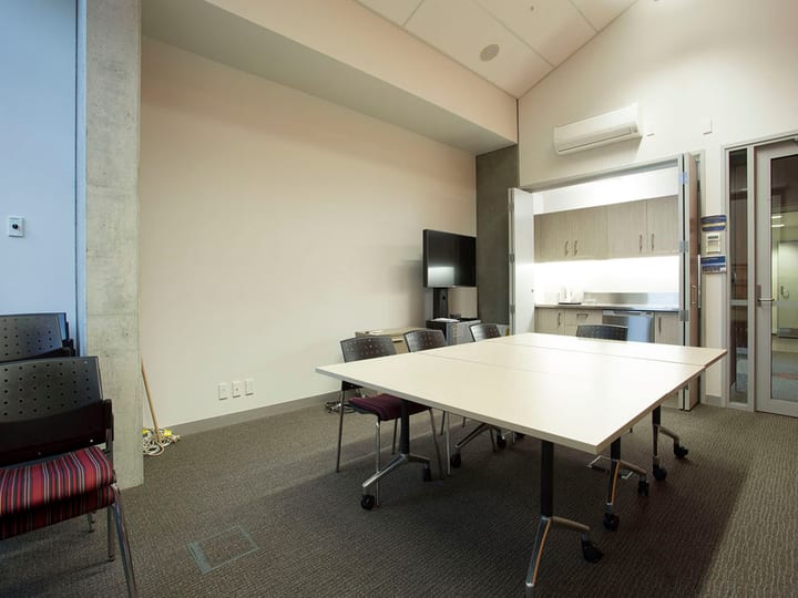 Meeting room with table, chairs, TV screen and kitchenette bench