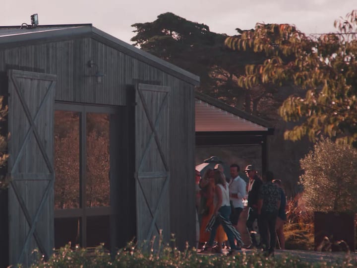 Dark timber clad barn building with large doors, surrounded by trees at golden hour
