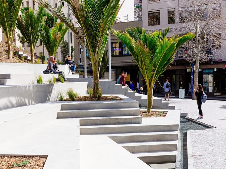 Stepped concrete terraces with trees in a city plaza, pedestrians in background