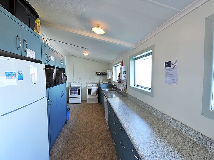 Hall kitchen with blue cabinetry, stoves, fridge and bench counter
