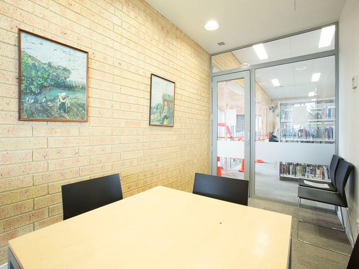 Small meeting room with table, chairs, and paintings on brick wall