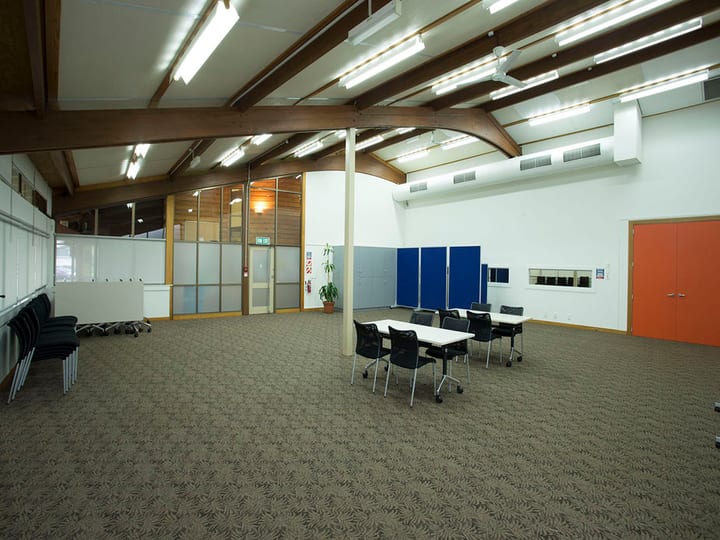 Community hall with curved timber-beam roof and tables arranged for a session