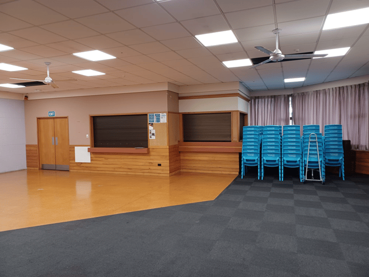 Empty hall with mixed floor surfaces, wooden bar servery and stacked blue chairs