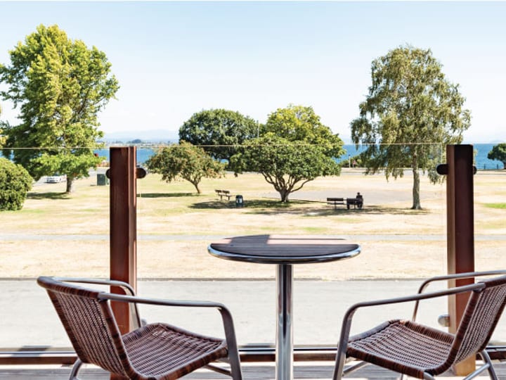 Balcony terrace with two rattan chairs and round table, overlooking park and lake