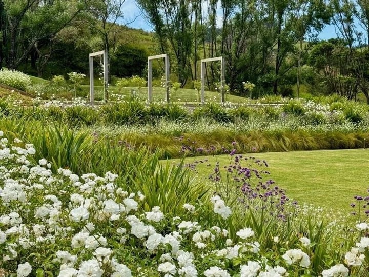 Landscaped gardens with white flower borders, ornamental grasses and timber arch frames on a lawn
