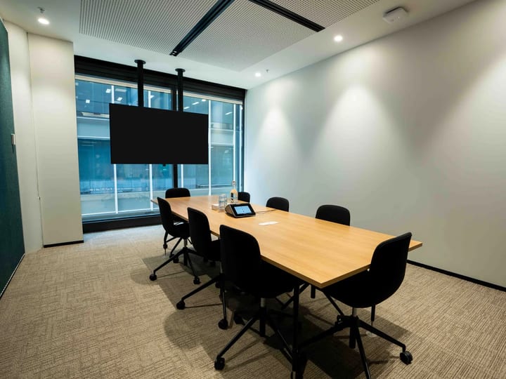 Meeting room with timber-topped table, black chairs, ceiling-mounted screen, and floor-to-ceiling city-view windows