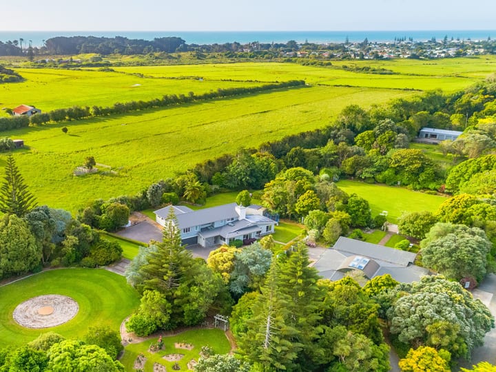 Aerial view of house and grounds surrounded by trees and farmland with coast in background