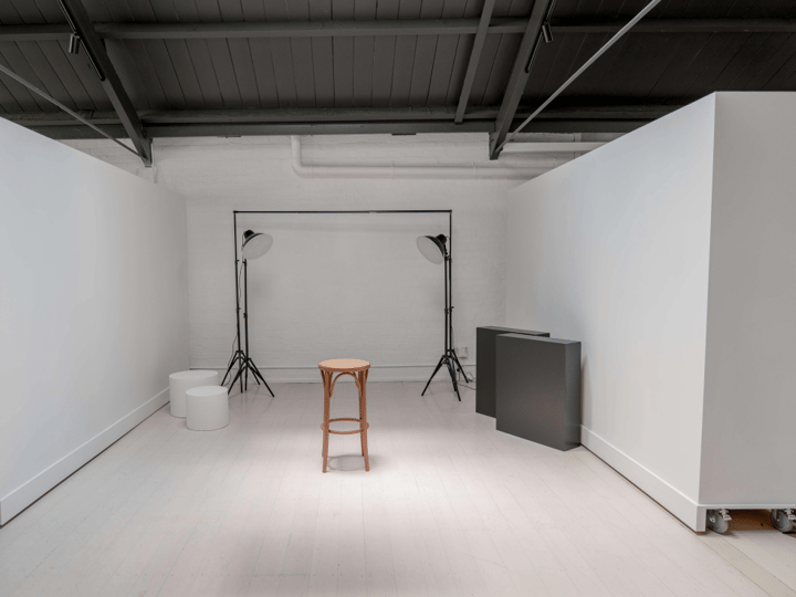White photography studio with movable white panels, two studio lights, and a single stool