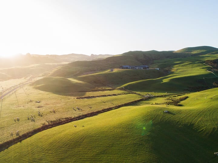 Aerial view of rolling green farmland and road at sunset, building barely visible in distance