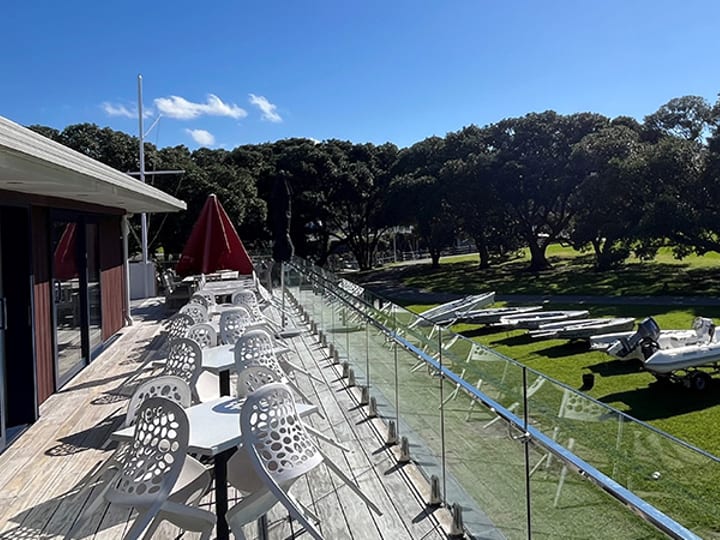 Outdoor deck with white chairs and tables overlooking lawn and boats