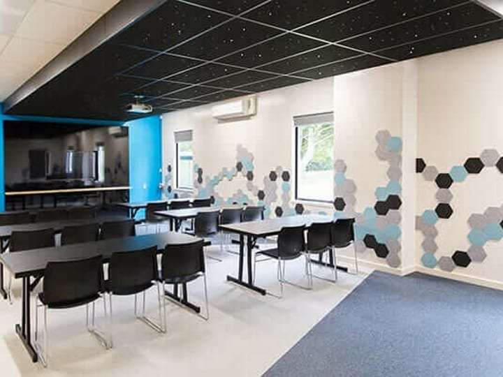Meeting room with rows of black tables and chairs, projection screen, and hexagon wall graphics