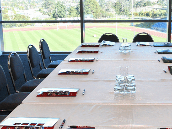 Boardroom table set with chairs and materials overlooking a sports field through windows