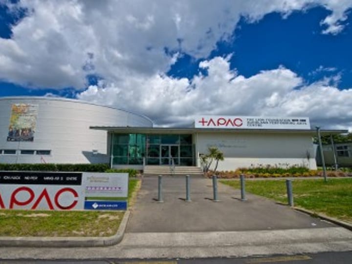 Performing arts centre exterior with cylindrical curved facade and centre signage under blue sky
