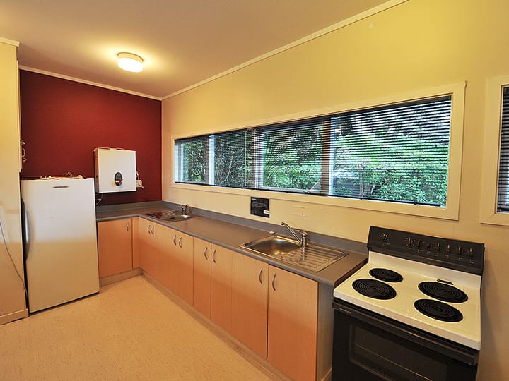 Kitchen with timber cabinetry, stove, and long window overlooking trees