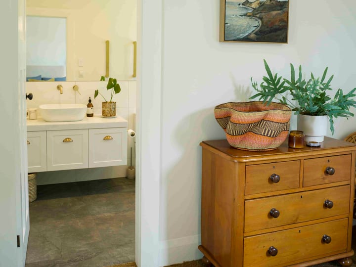 Bedroom with timber dresser, wall art and view into an ensuite bathroom