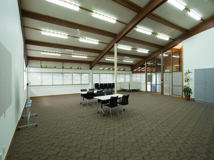 Large community room with exposed timber-beam roof, carpet, and table cluster