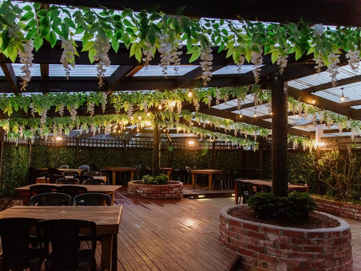 Covered outdoor deck with timber tables, hanging foliage and festoon lighting at night