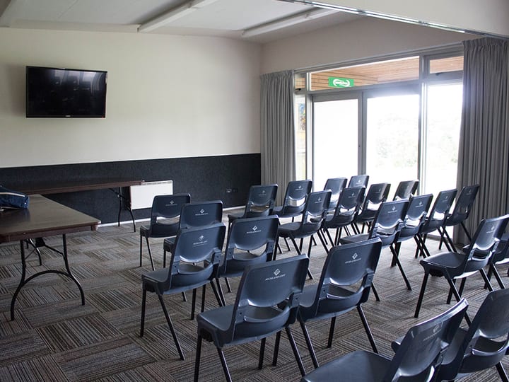 Meeting room with rows of chairs, large windows and a wall-mounted screen
