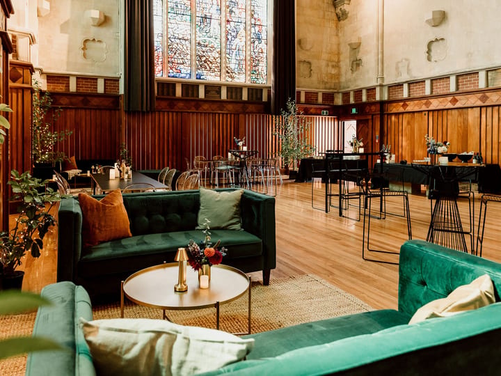 Historic hall interior with dark timber panelling, stained glass windows and lounge seating