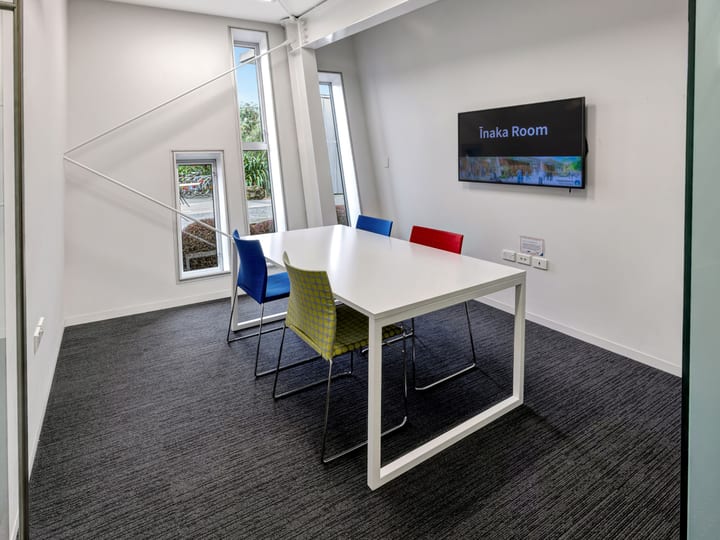 Small meeting room with white table, coloured chairs and wall-mounted screen