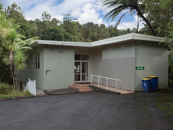 Single-storey community hall with vertical cladding and access ramp surrounded by trees