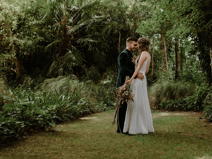 Two people embracing in a dense garden clearing surrounded by trees and lush planting