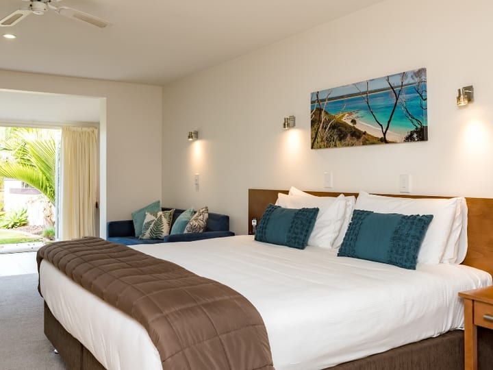King bedroom with teal cushions, wall art, and sliding doors to garden terrace