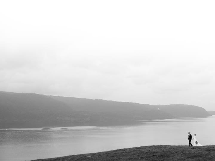 Two figures on grassy hillside beside a lake with misty hills, black and white landscape