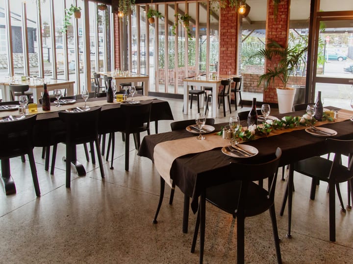 Brick and glass dining room with set long tables, concrete floor, and street view