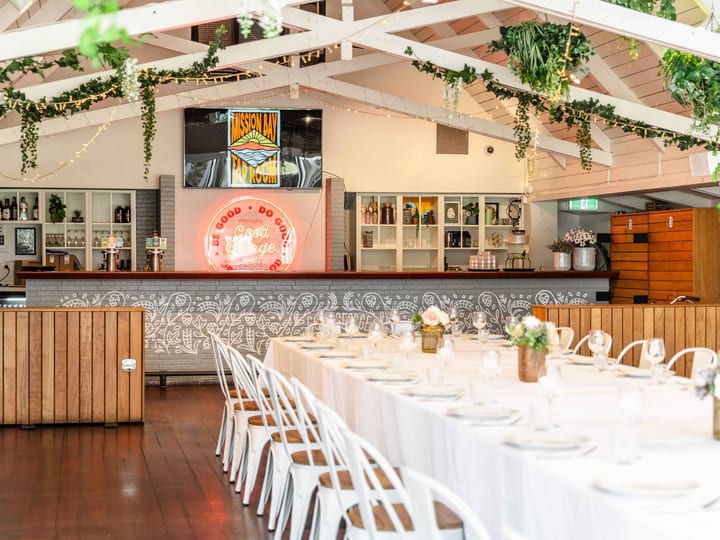 Function hall with vaulted white timber ceiling, neon bar sign and round tables set for dining
