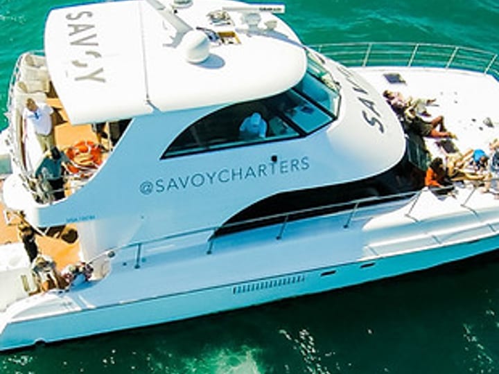 White motor vessel viewed from above on open water, with people on deck