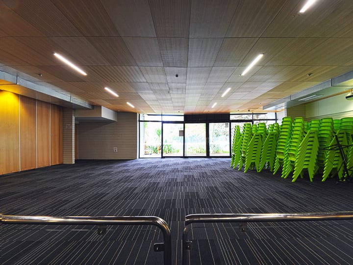 Large function hall with timber ceiling, green stacked chairs and glass doors