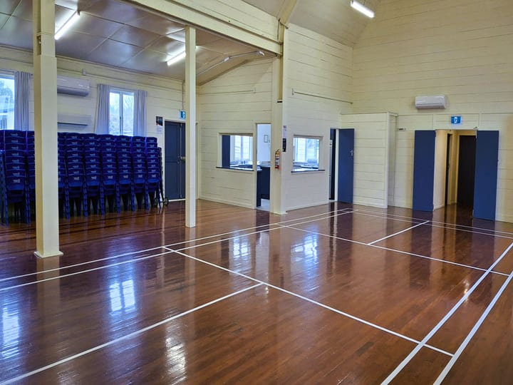 Hall interior with polished timber floor and stacked chairs, second room visible