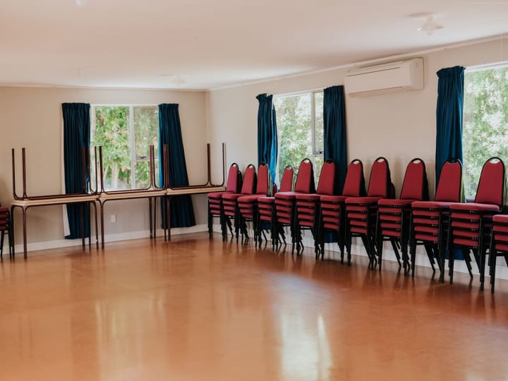Plain hall room with stacked chairs, trestle tables and blue curtains