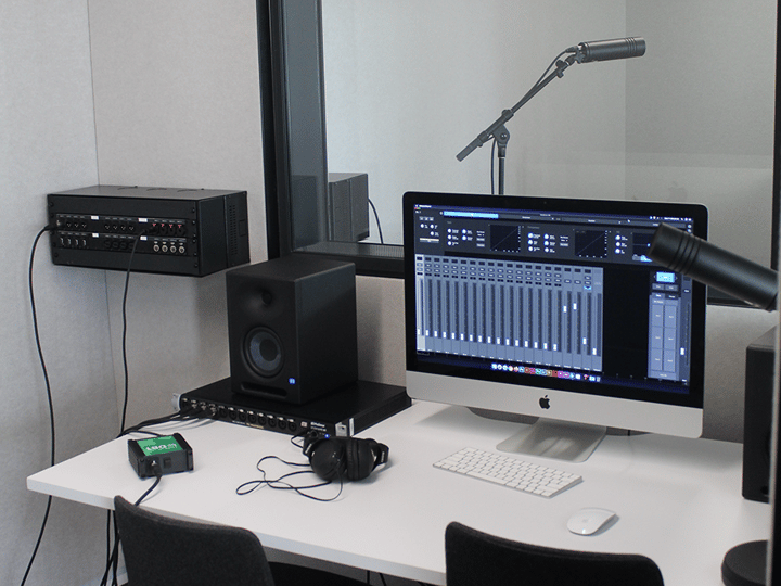 Small recording studio booth with microphone, monitors and computer