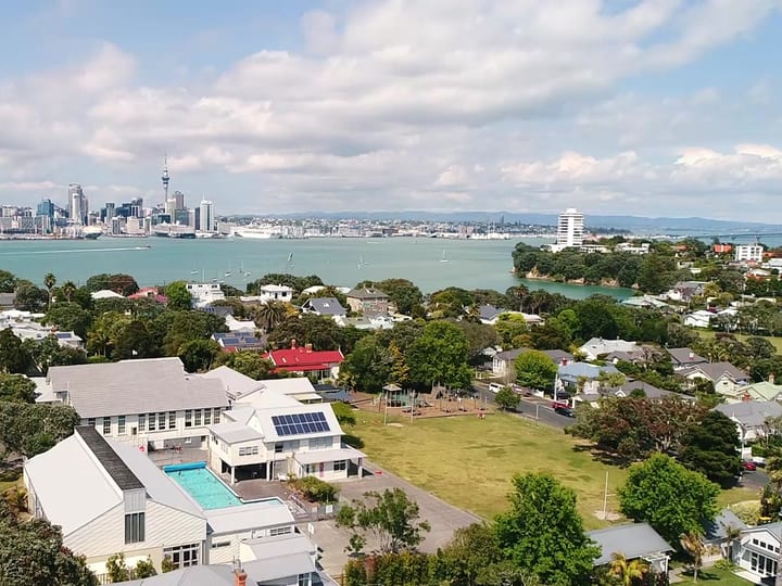 Aerial view of school buildings and pool with harbour and city skyline behind