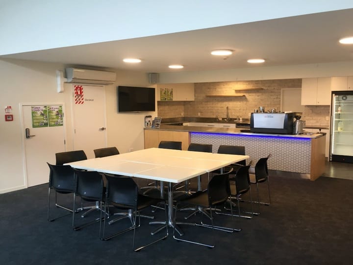 Small room with a white table, dark chairs, kitchen counter with appliances, and a TV on the wall