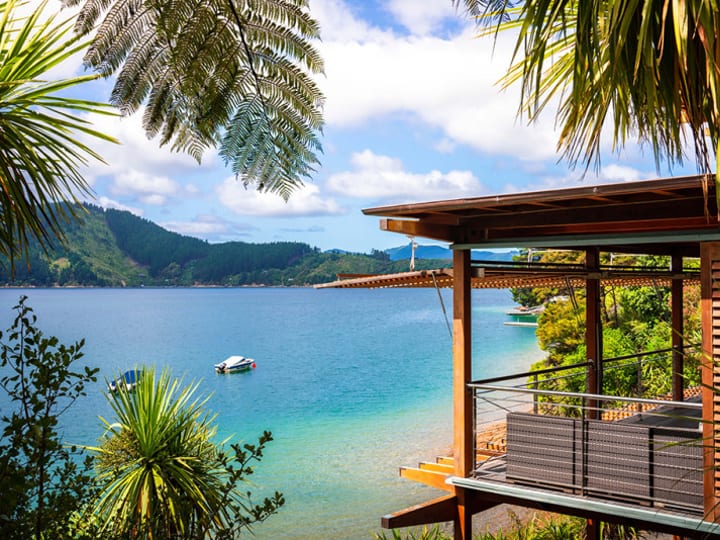 Waterfront timber lodge building with a deck and jetty, surrounded by native bush and a sheltered cove
