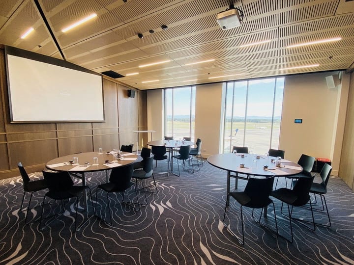 Timber-panelled meeting room with round tables, black chairs, projection screen, and large windows