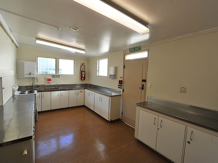 Plain hall kitchen with stainless steel benchtops, white cabinets and electric stove