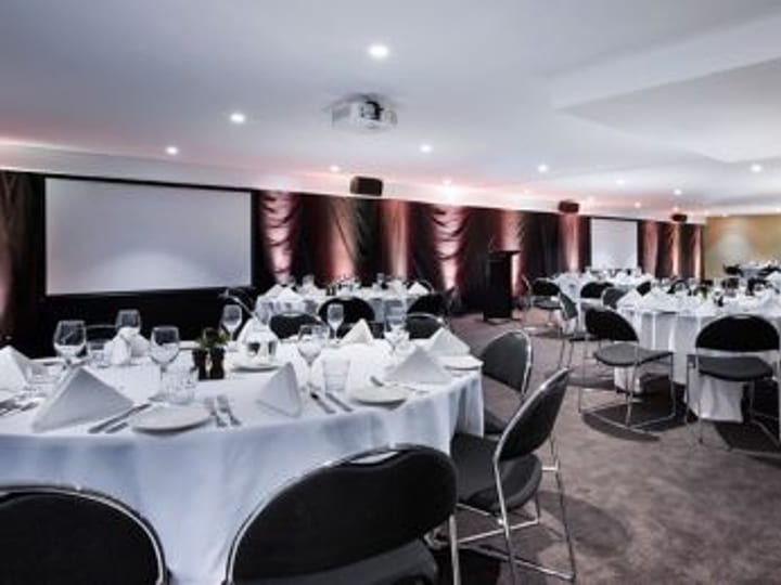 Banquet room set with round tables, white napkins, and projection screen