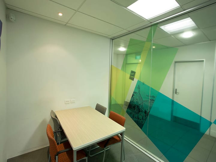 Small meeting room with timber table, chairs, and colourful graphic glass partition