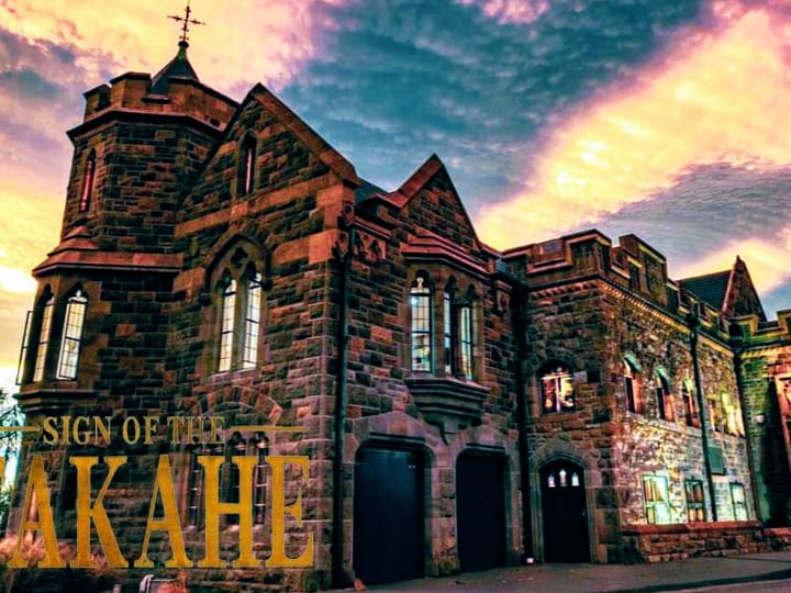 Gothic stone building with turrets, arched windows and a central tower, lit at dusk against a dramatic sky