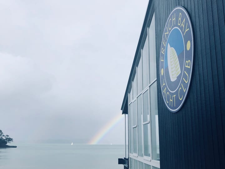 Dark blue clubhouse exterior with circular logo and rainbow over water