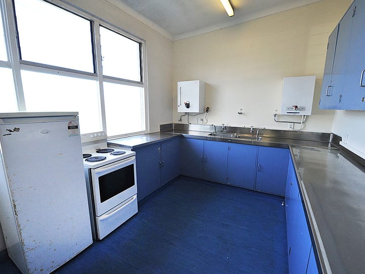 Compact kitchen with blue cabinetry, stainless bench, freestanding cooker and refrigerator