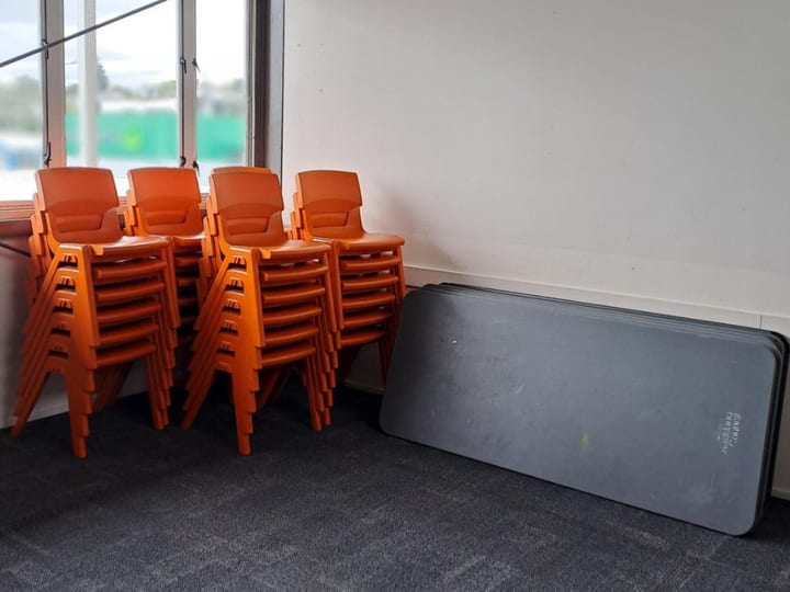 Empty room with stacked orange chairs and folded tables on a carpeted floor
