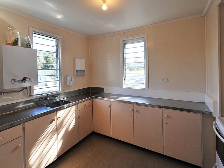 Small kitchen with pink cabinets, stainless benches, and louvre windows