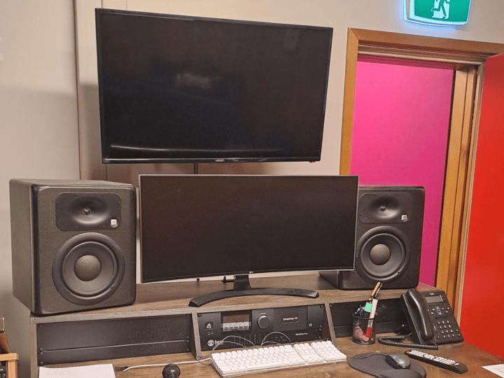 Studio control desk with two monitors, mixing equipment, and speakers