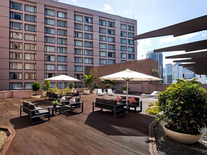 Elevated outdoor timber deck with lounge furniture, white umbrellas, and city buildings behind